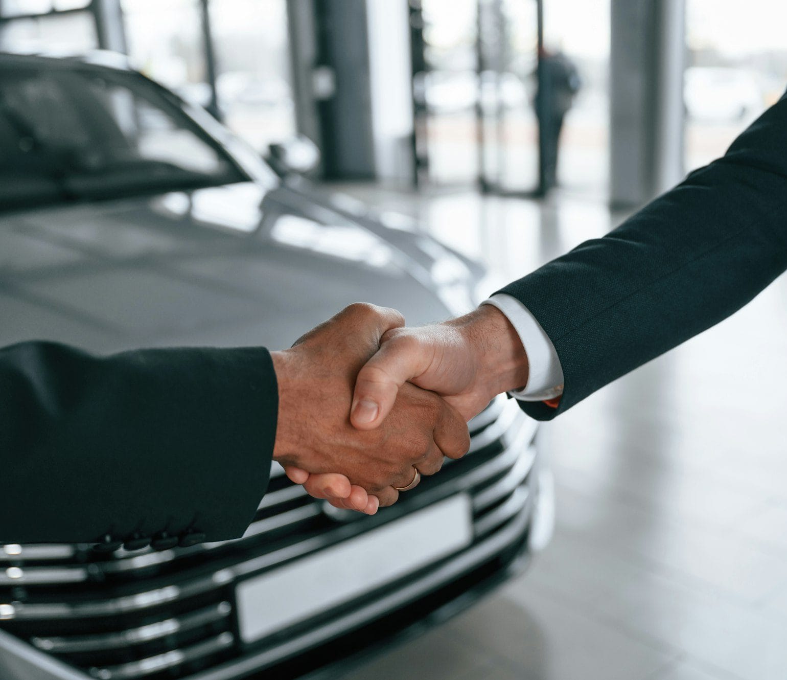 Two businessmen are standing in the car showroom and making a deal, handshake